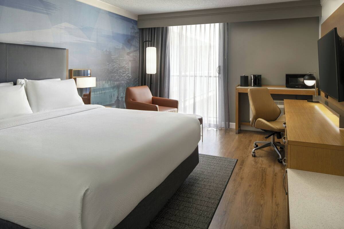 A hotel room with a large bed, a desk with a computer, a chair, and a TV.
