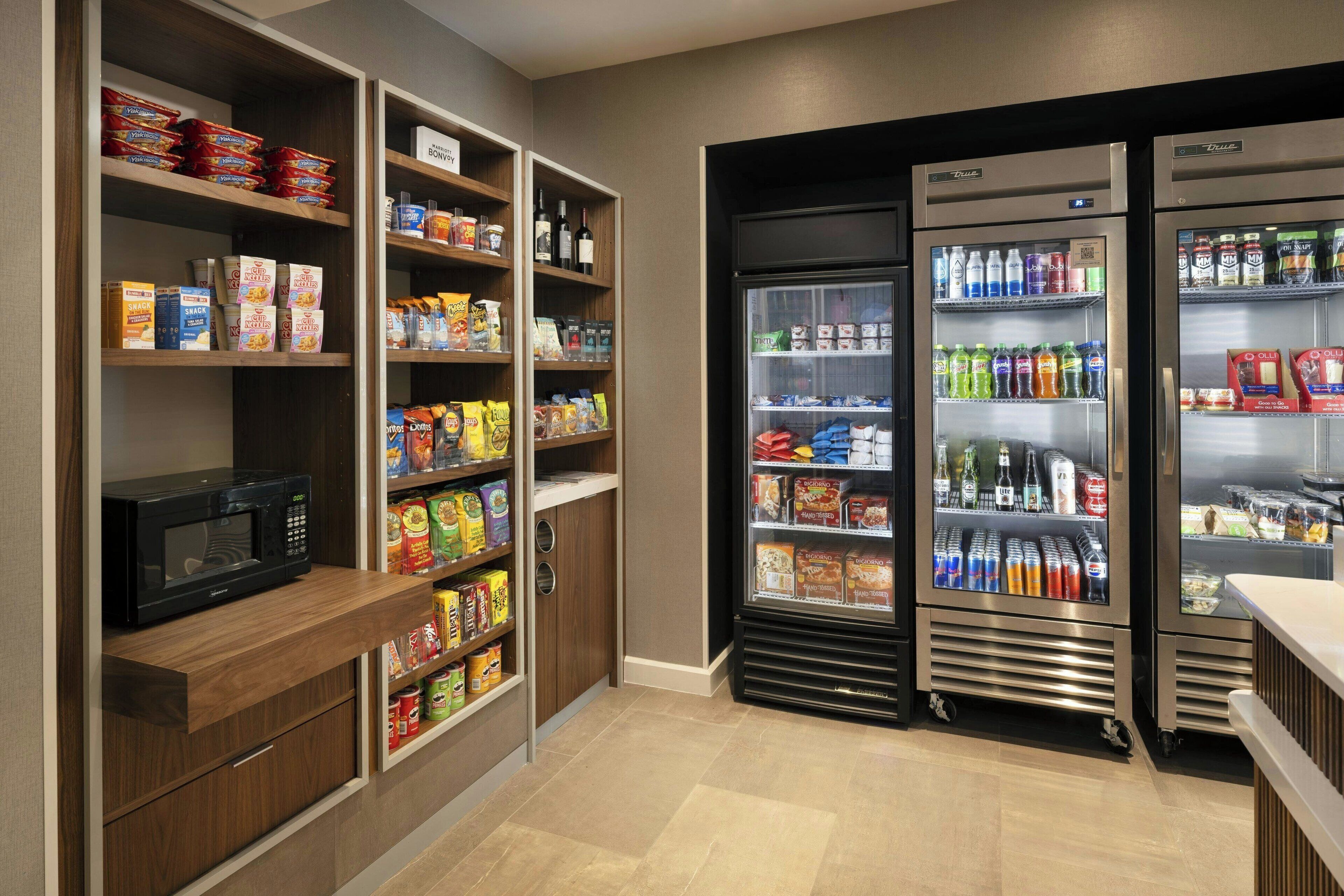 A self-service food area with microwaves, refrigerated beverage dispensers, and shelves stocked with snacks and beverages.