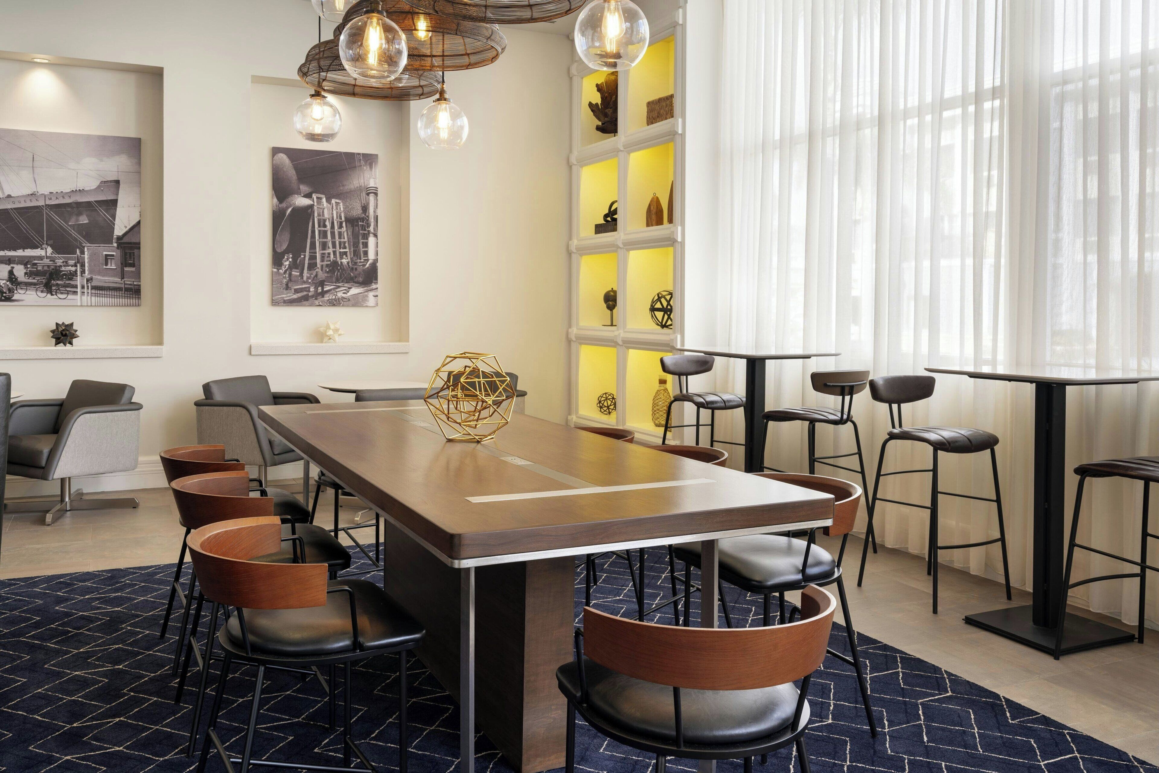 Uma sala de jantar moderna com uma mesa comprida, várias cadeiras e iluminação pendente.