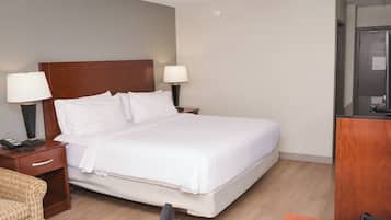 Quarto de hotel com uma cama grande, duas luminárias de cabeceira, uma cabeceira de madeira, uma mesa de cabeceira com um telefone, uma pequena mesa e um armário de madeira.