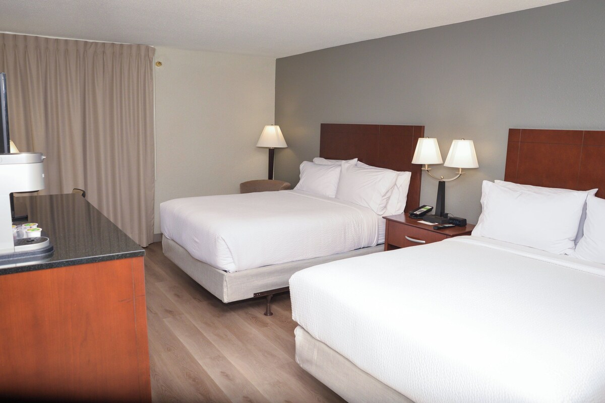 Ein Hotelzimmer mit zwei Betten, einem Schreibtisch und einem Sessel. Es gibt zwei Nachttische mit Lampen.