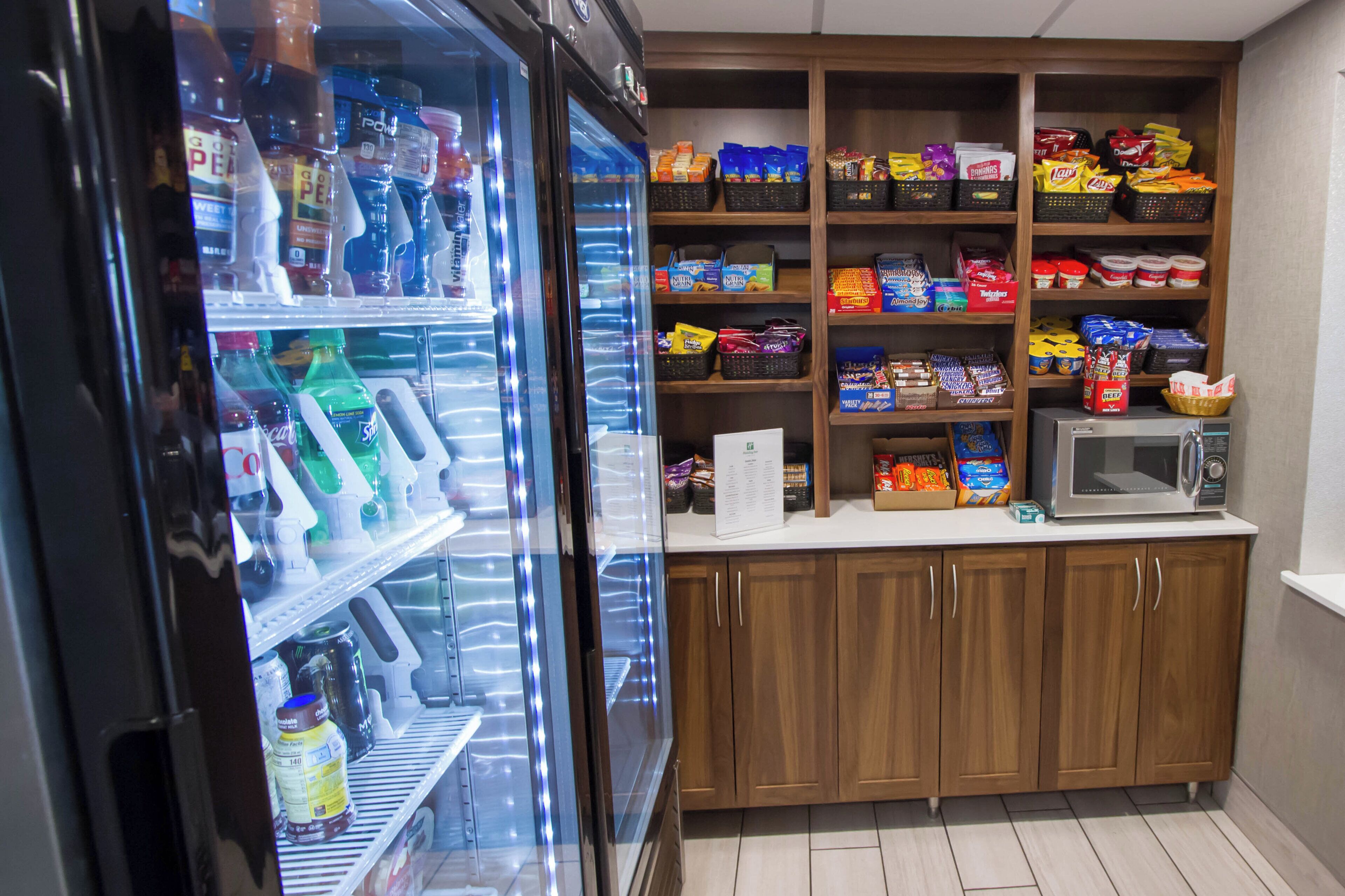 A small kitchenette area with a refrigerator stocked with beverages and snacks, a microwave, and wooden cabinets above.
