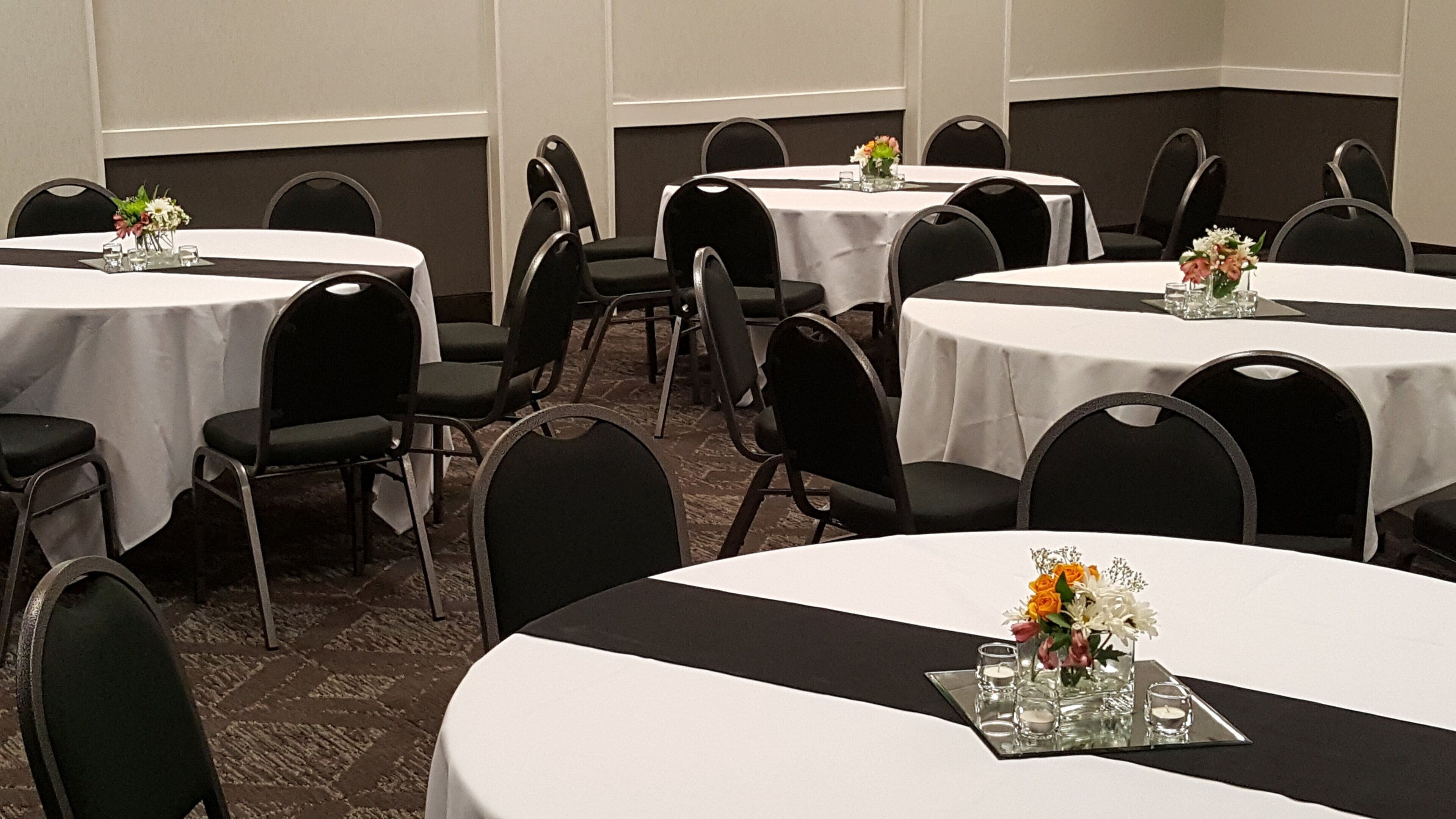 A conference room with round tables, black chairs, and white tablecloths.