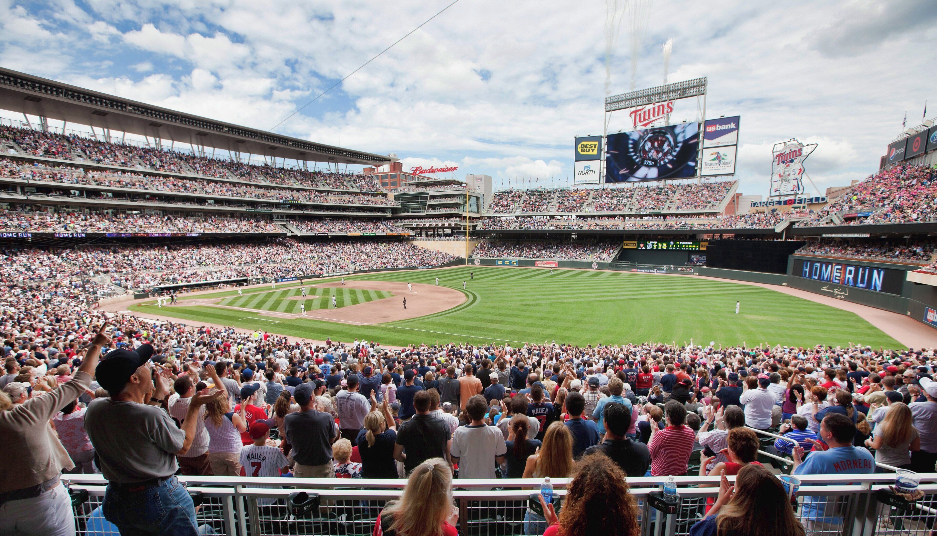 A baseball stadium with multiple levels of seating, a large screen displaying the team name, and a clear sky.