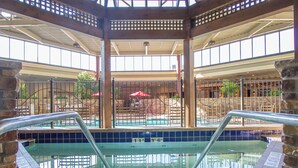 Une piscine intérieure à l’eau claire, entourée de piliers en pierre et surmontée d’une structure de plafond en bois.