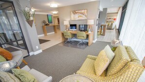 Un hall d’hôtel moderne doté d’un espace salon, d’un bureau avec des ordinateurs et d’une grande fenêtre.