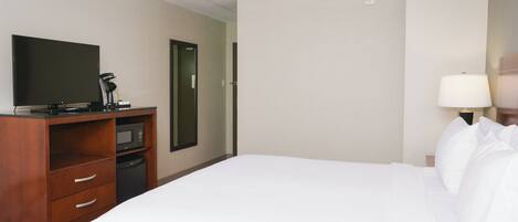 A hotel room with a bed, a TV, a microwave, a desk with drawers, and a lamp.