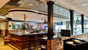 Un espace bar avec un comptoir en bois, des tabourets de bar et un écran de télévision.