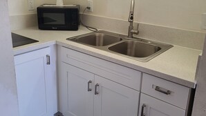 A compact kitchen with a microwave, two sinks, and white cabinetry. - Relax Inn And Suites (El Cajon)