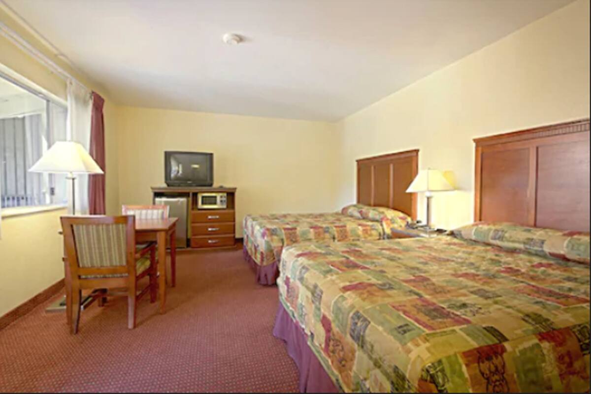 A hotel room with two beds, a desk, a television, and a dresser.