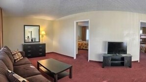 A hotel room with a living area featuring a sofa, a coffee table, a TV, and a small dining table with chairs. - Relax Inn And Suites (El Cajon)
