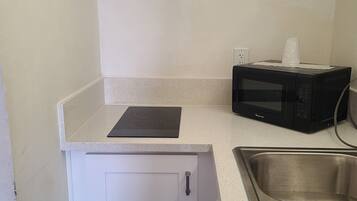 A kitchenette with a stainless steel sink, a microwave, and a white cabinet.