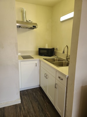 A compact kitchen with white cabinets, a microwave, a stainless steel sink, and a ventilation hood. - Relax Inn And Suites (El Cajon)