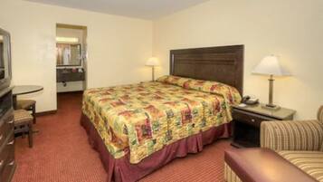 A hotel room with a bed, bedside table, lamp, chair, and a dresser.