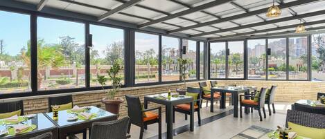 A restaurant with outdoor seating, large windows, and a view of the cityscape.