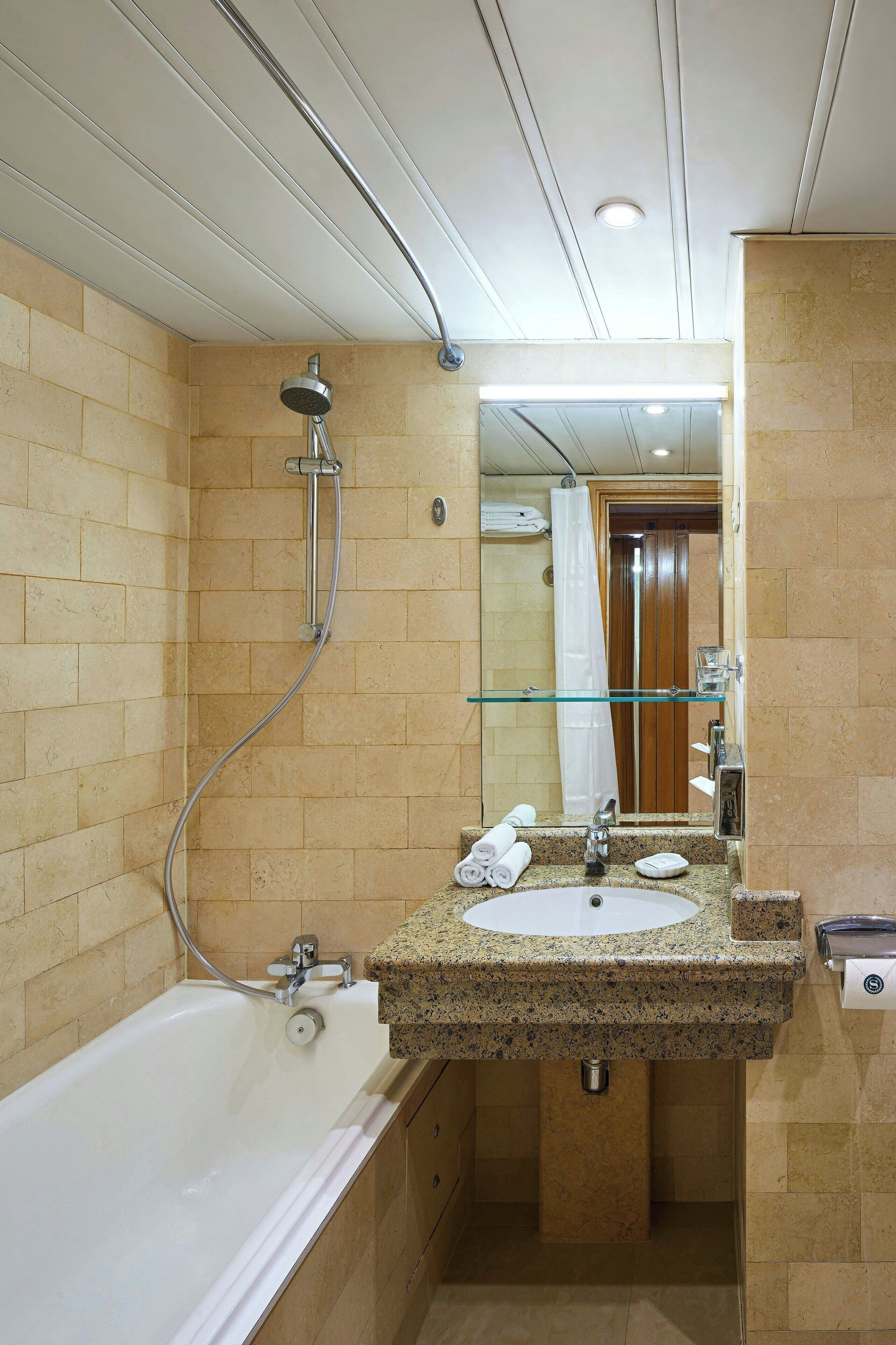 A modern bathroom with a glass shower enclosure, a granite countertop sink, and a mirror above it.