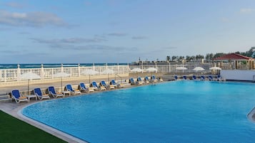Una piscina al aire libre, sombrillas, sillones reclinables de piscina