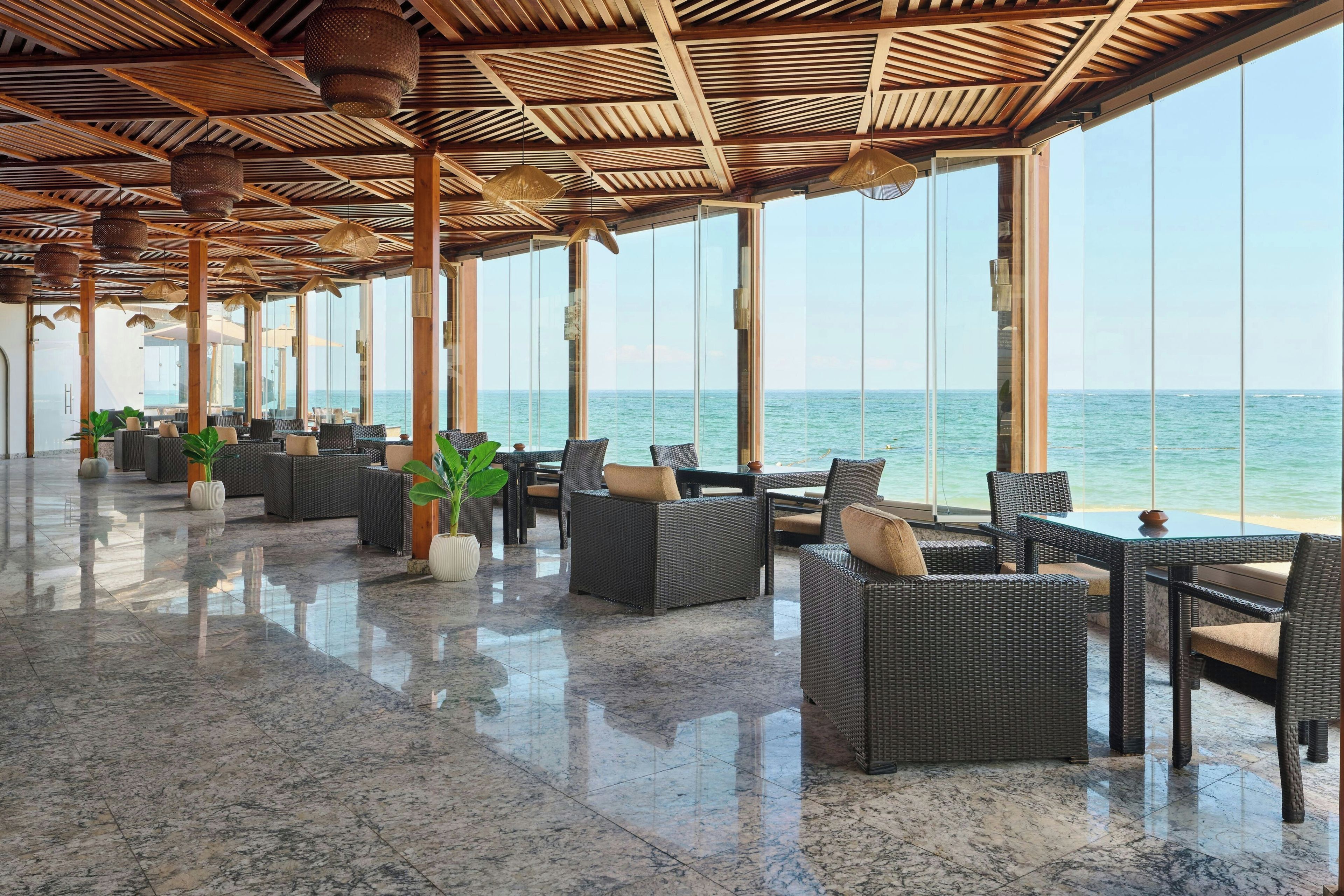 A spacious indoor area with a view of the sea, featuring wicker furniture and a polished marble floor.