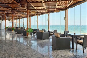 A spacious indoor area with a view of the sea, featuring wicker furniture and a polished marble floor.