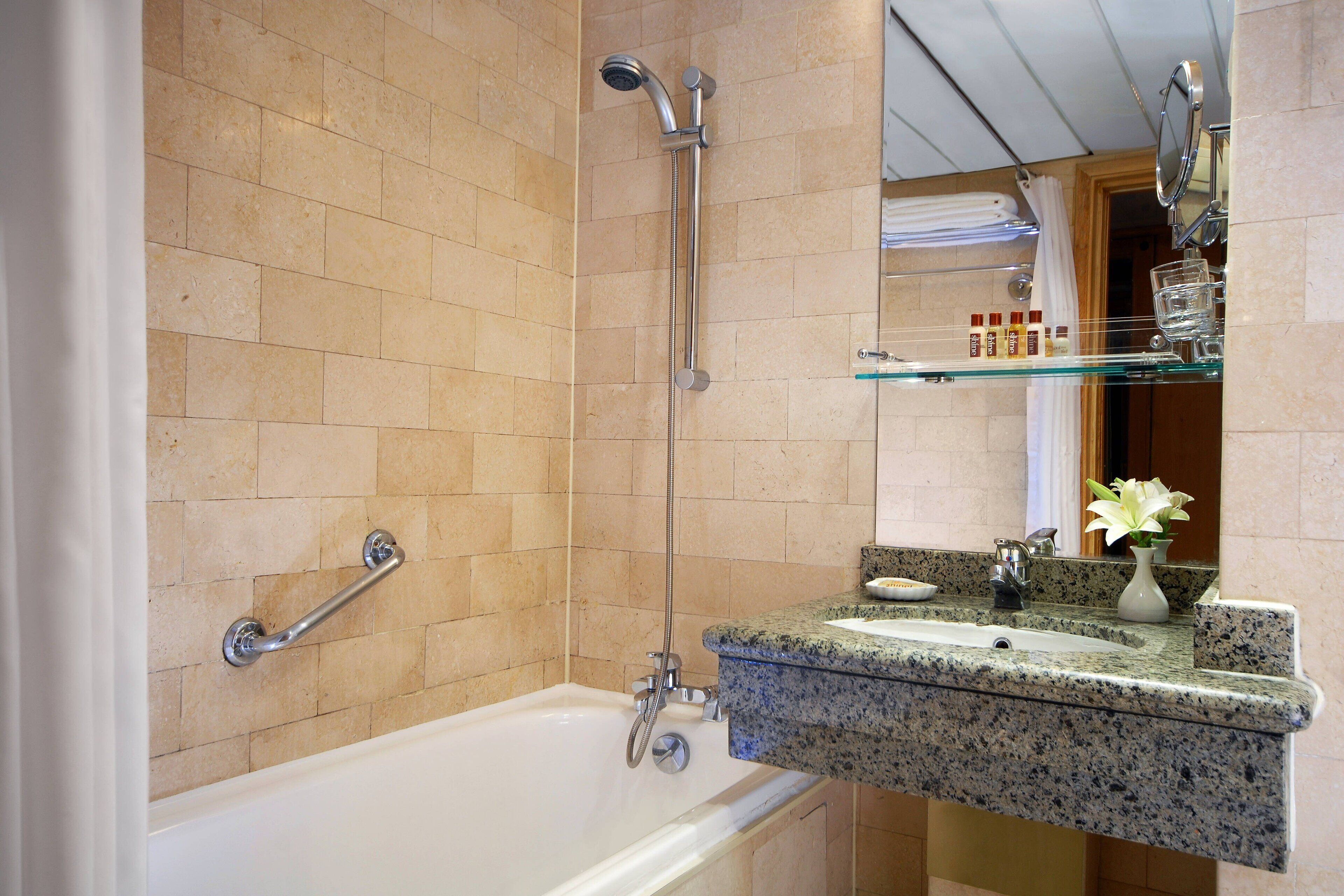 A bathroom with a bathtub, a glass shelf with toiletries, and a mirror.