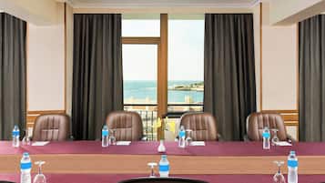 A conference room with a view of the sea, equipped with water bottles, wine glasses, and a vase with flowers.