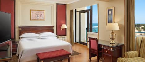 Une chambre d’hôtel avec un grand lit, un bureau, une chaise, une télévision et une vue sur l’océan.