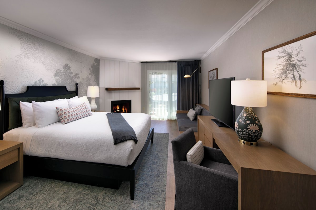 A modern hotel room with a large bed, bedside tables, a TV, and a fireplace.