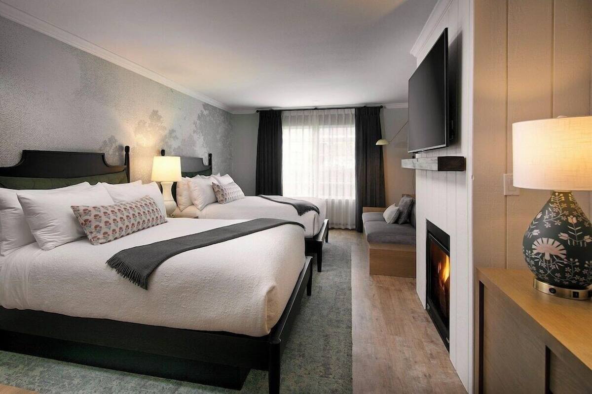 A hotel room with two beds, a TV, a fireplace, and a lamp.