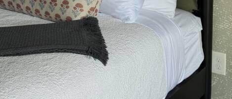 A bed with a dark headboard, white and patterned pillows, and a gray throw blanket.