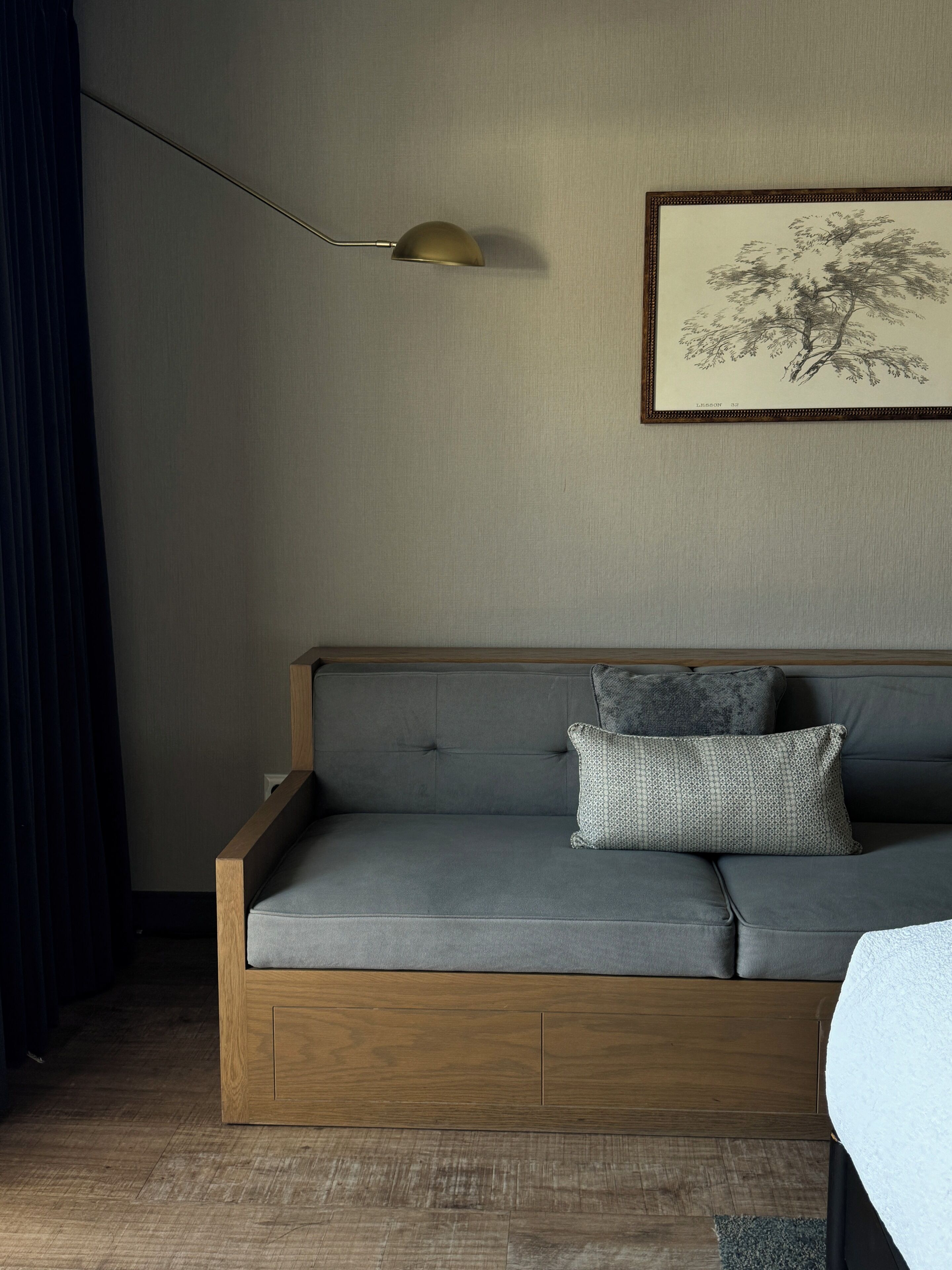 A modern living room with a grey sofa, wooden frame, and a single gold-colored floor lamp.