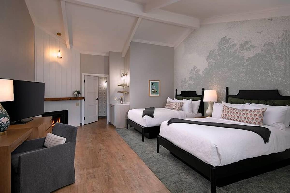 A hotel room with two beds, a TV, a sofa, and a fireplace.