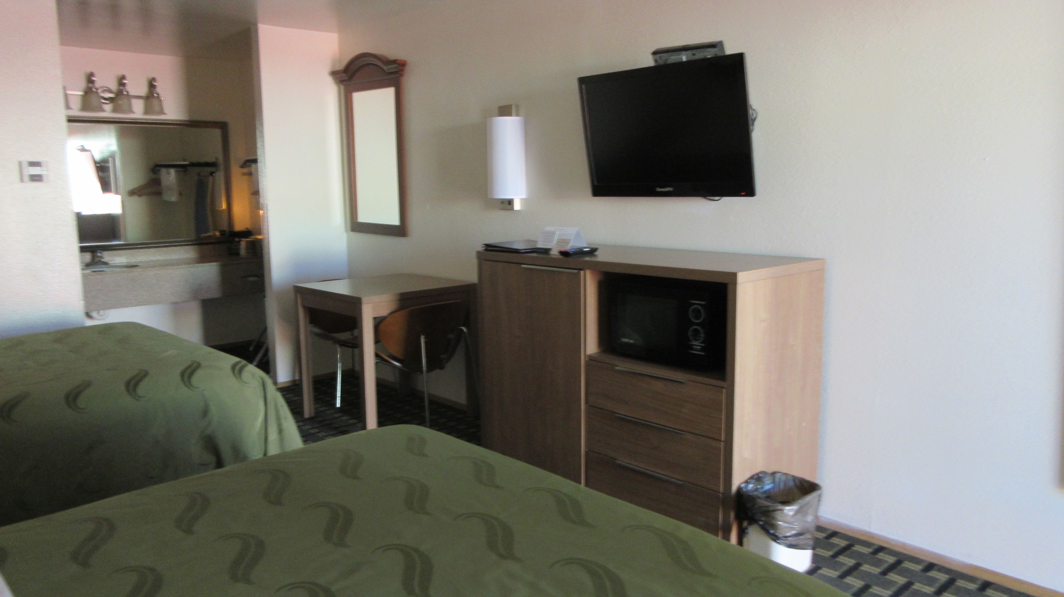 Una camera d'albergo con un letto, una scrivania, una sedia, una televisione e un cestino.