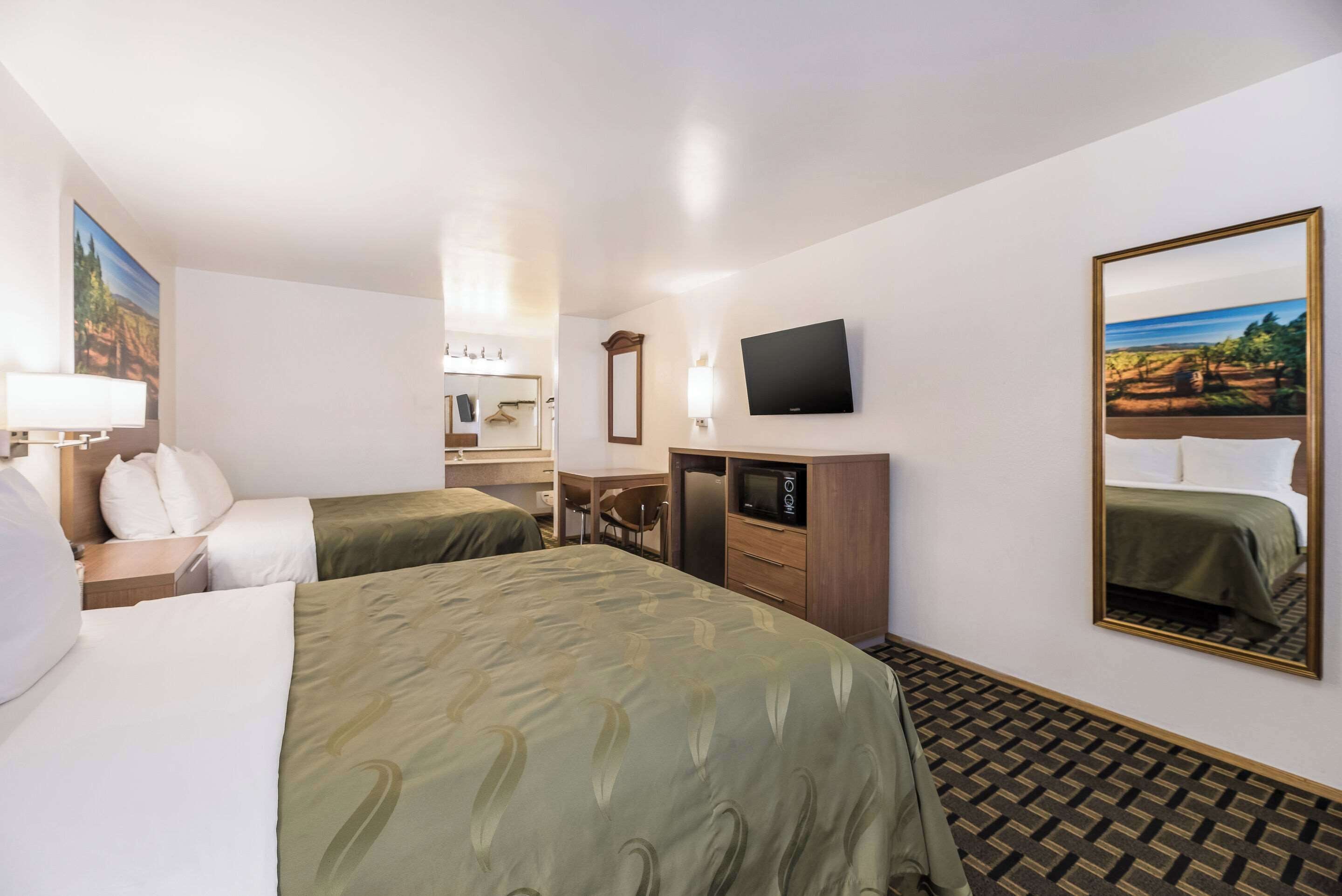 A hotel room with two beds, a TV, a desk, and a mirror.