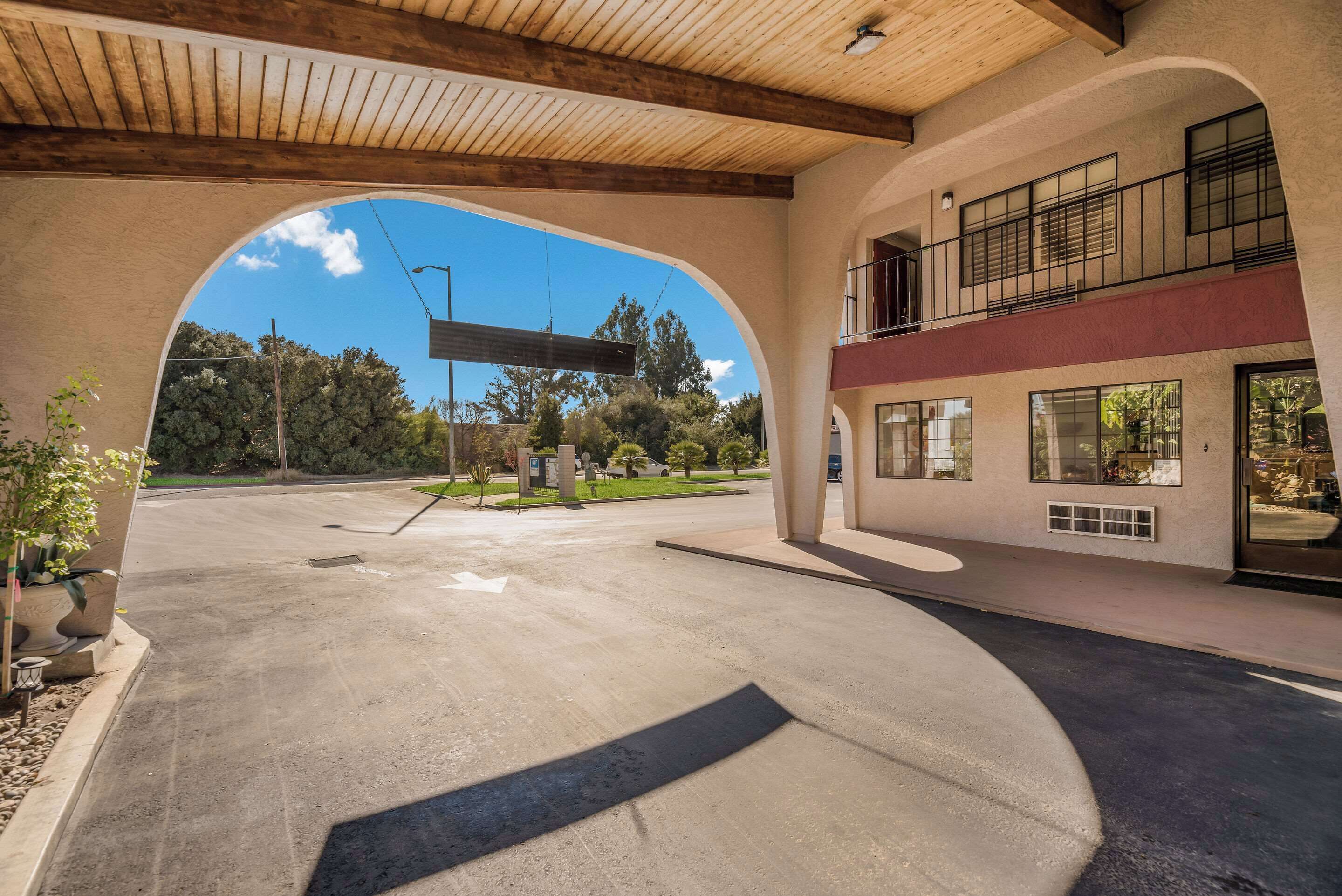 A spacious outdoor area with a concrete floor, a wooden ceiling, and a view of a building with large windows and a balcony.