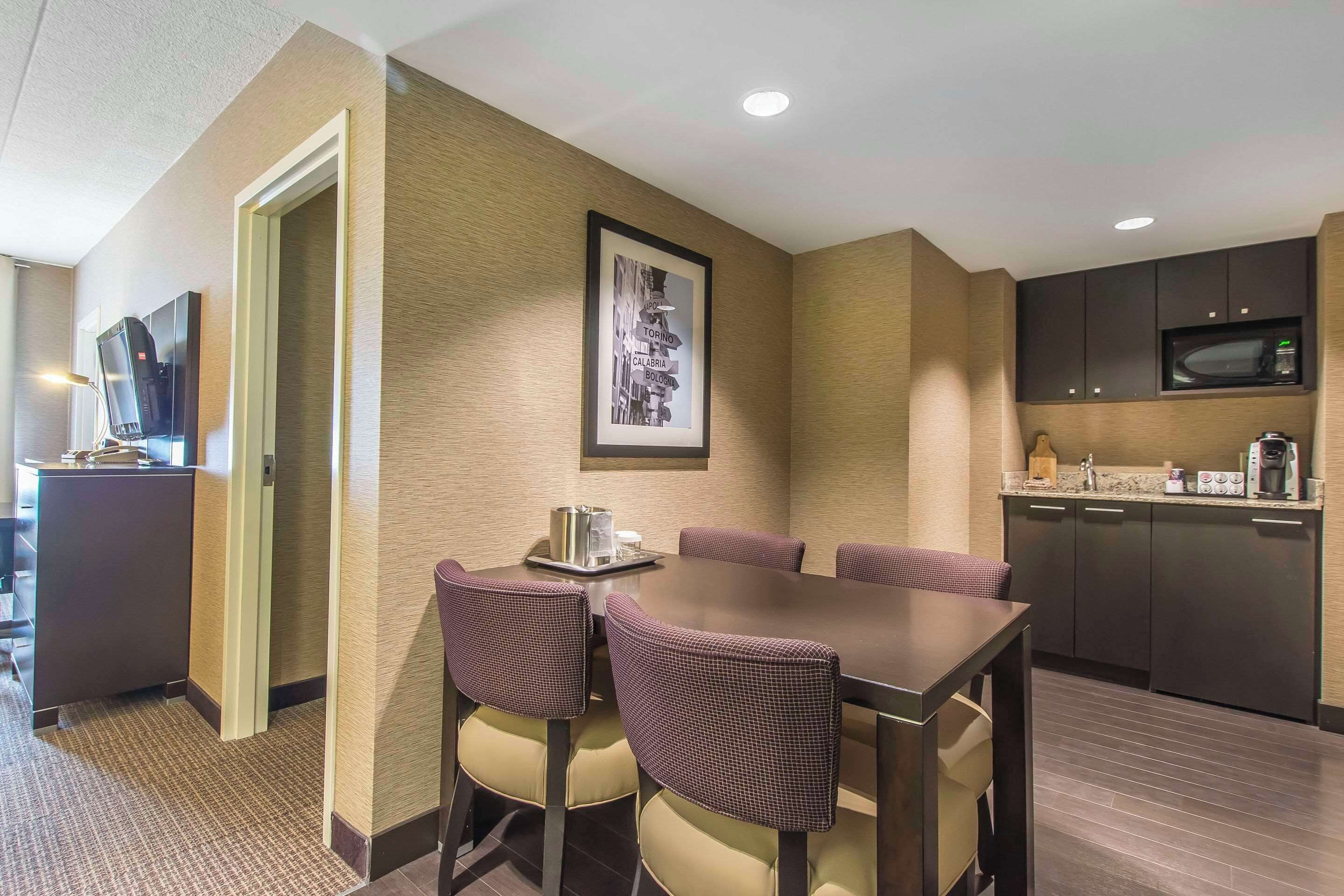 A hotel room with a dining table, chairs, a television, a framed picture on the wall, a microwave, and a coffee maker.