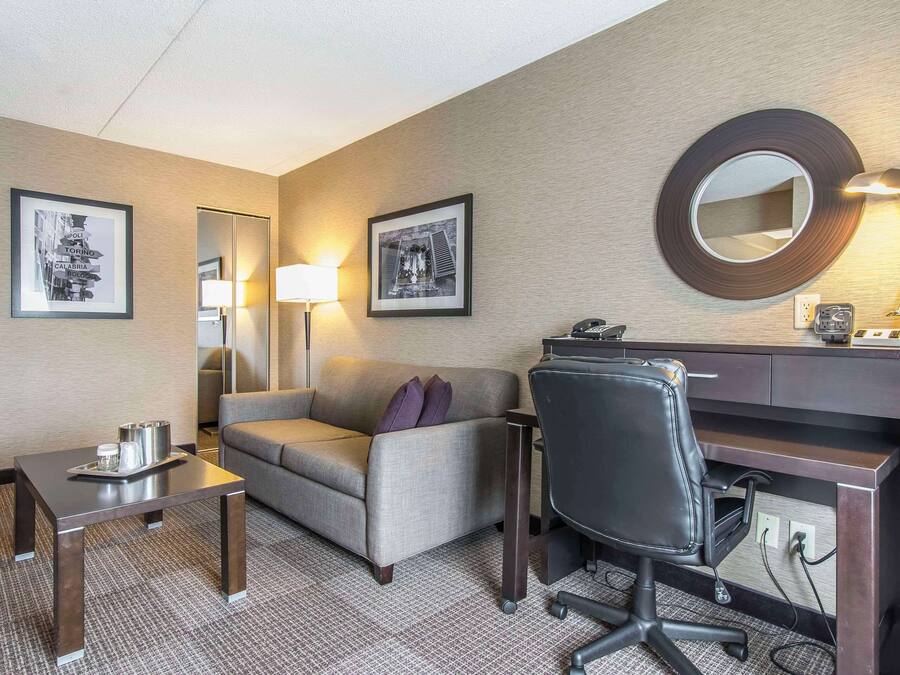 Habitación de hotel con escritorio, sofá, silla, lámpara y cuadros en las paredes.