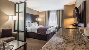 Quarto de hotel com cama, escrivaninha, televisão e janela com cortinas.