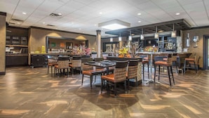 Uma área de bar espaçosa com banquetas altas e um balcão comprido, repleta de equipamentos de bar e plantas decorativas.