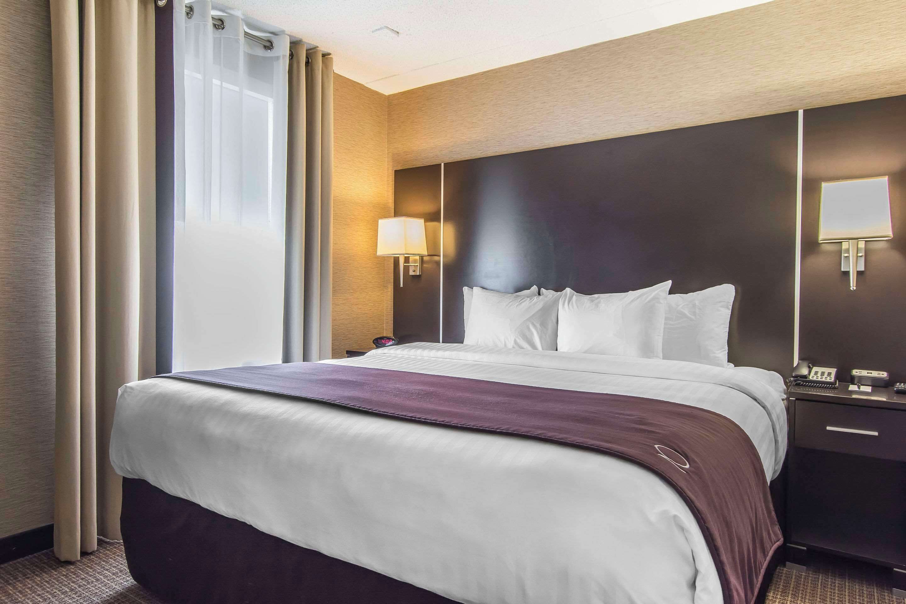 A hotel room with a large bed, a nightstand with a lamp, and a window with curtains.