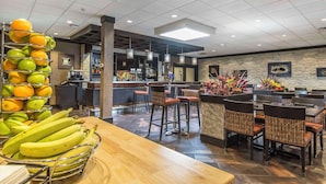 Restaurante com área de bar, mesas e cadeiras, e uma exposição de frutas.
