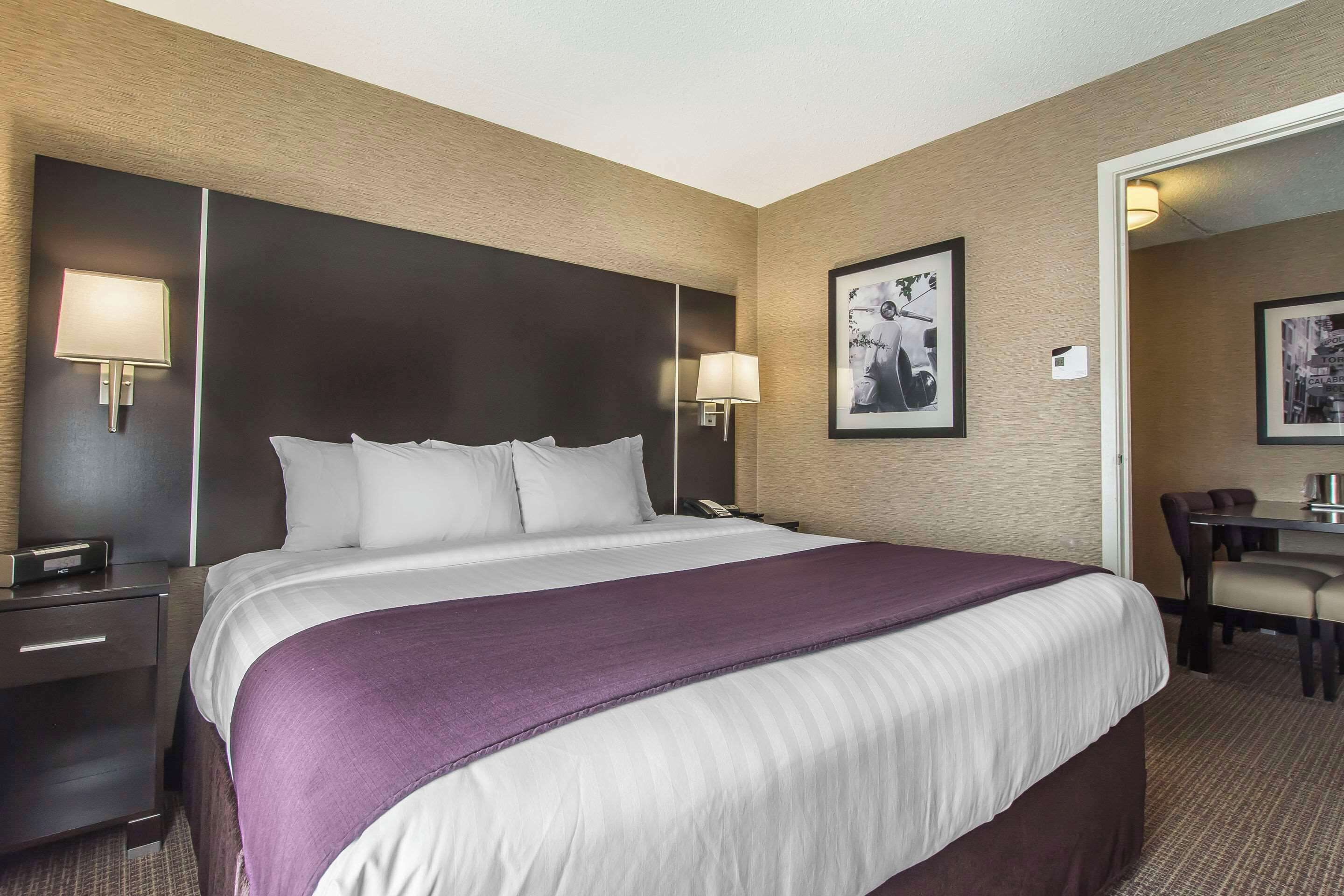 A hotel room with a large bed, two bedside lamps, a desk with a chair, and a framed picture on the wall.