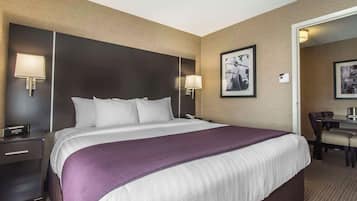 A hotel room with a large bed, two bedside lamps, a desk with a chair, and a framed picture on the wall.