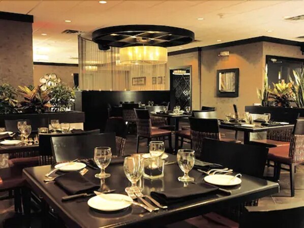 A restaurant with tables set for dining, featuring a modern interior with a chandelier and potted plants.