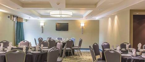 A conference room with round tables, chairs, and a television on the wall.