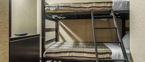 A bunk bed with a striped mattress and a ladder, a small desk with a remote control, and a carpeted floor.