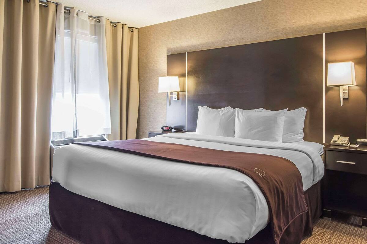 A hotel room with a large bed, two bedside lamps, a nightstand, and a window with curtains.
