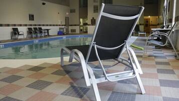 An indoor swimming pool with tiled flooring and several lounge chairs.