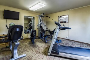 A gym with cardio machines, a mirror, a TV, and a bulletin board.
