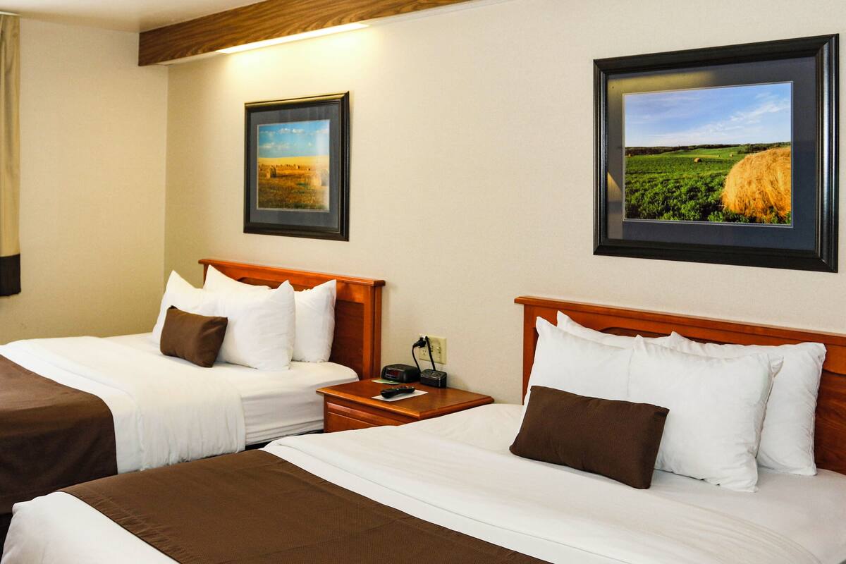 A hotel room with two beds, each with white and brown bedding, a wooden headboard, and a nightstand with a remote control.