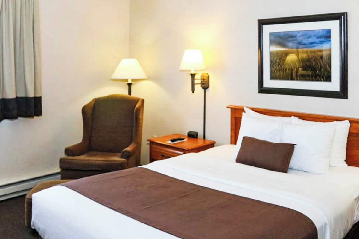A hotel room with a large bed, a chair, two bedside tables, a lamp, and a framed picture on the wall.